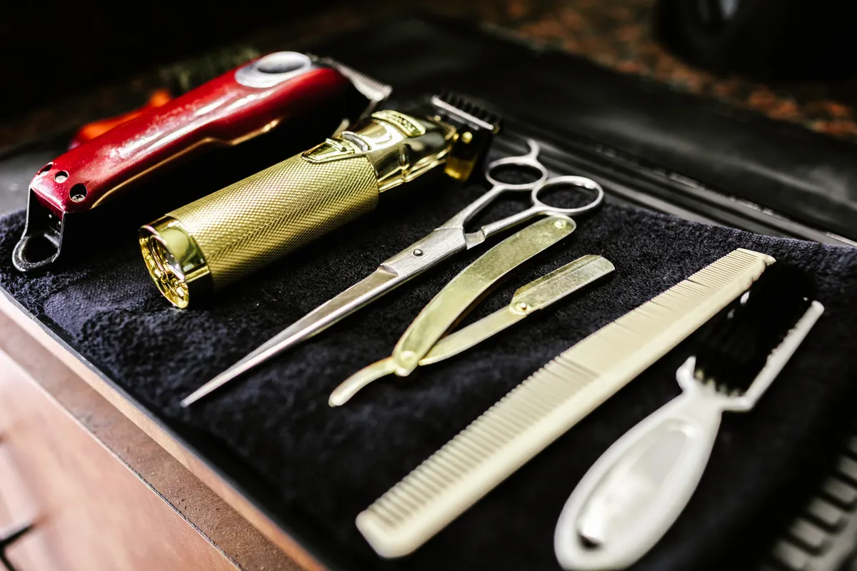 Clippers, scissors, a razor and combs arranged on a dark barber towel
