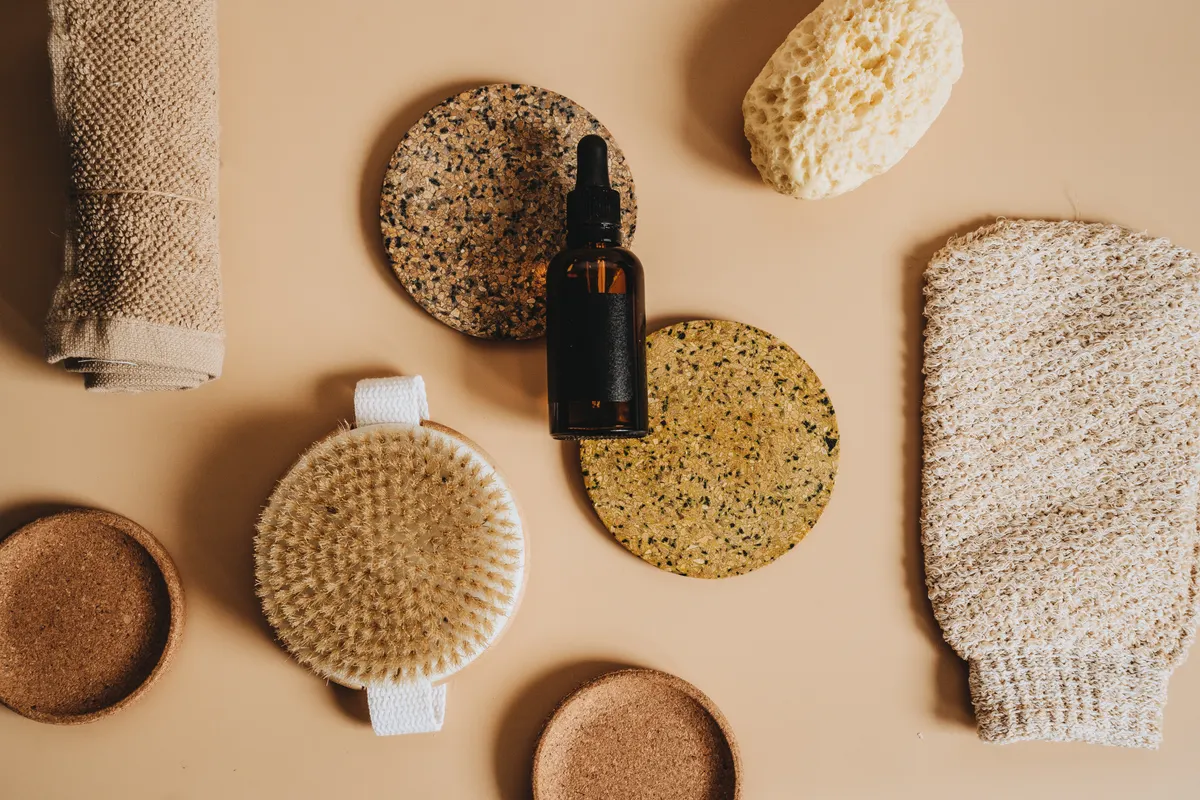 Body brush, towel, sponges and an amber bottle on a beige surface