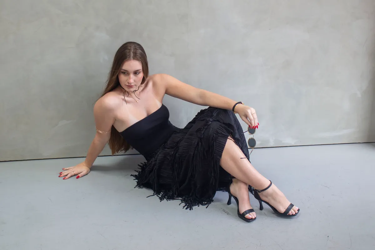 Woman in a black fringed dress and heels against a gray studio backdrop