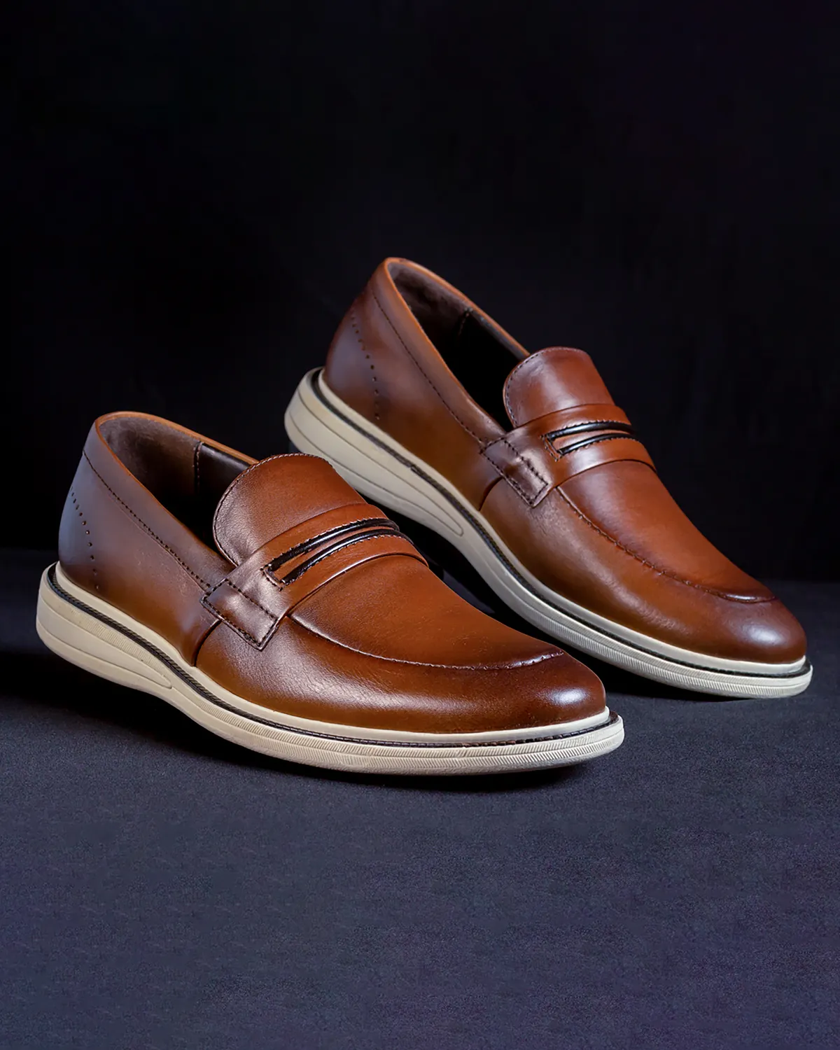 Brown leather loafers with pale soles against a dark background