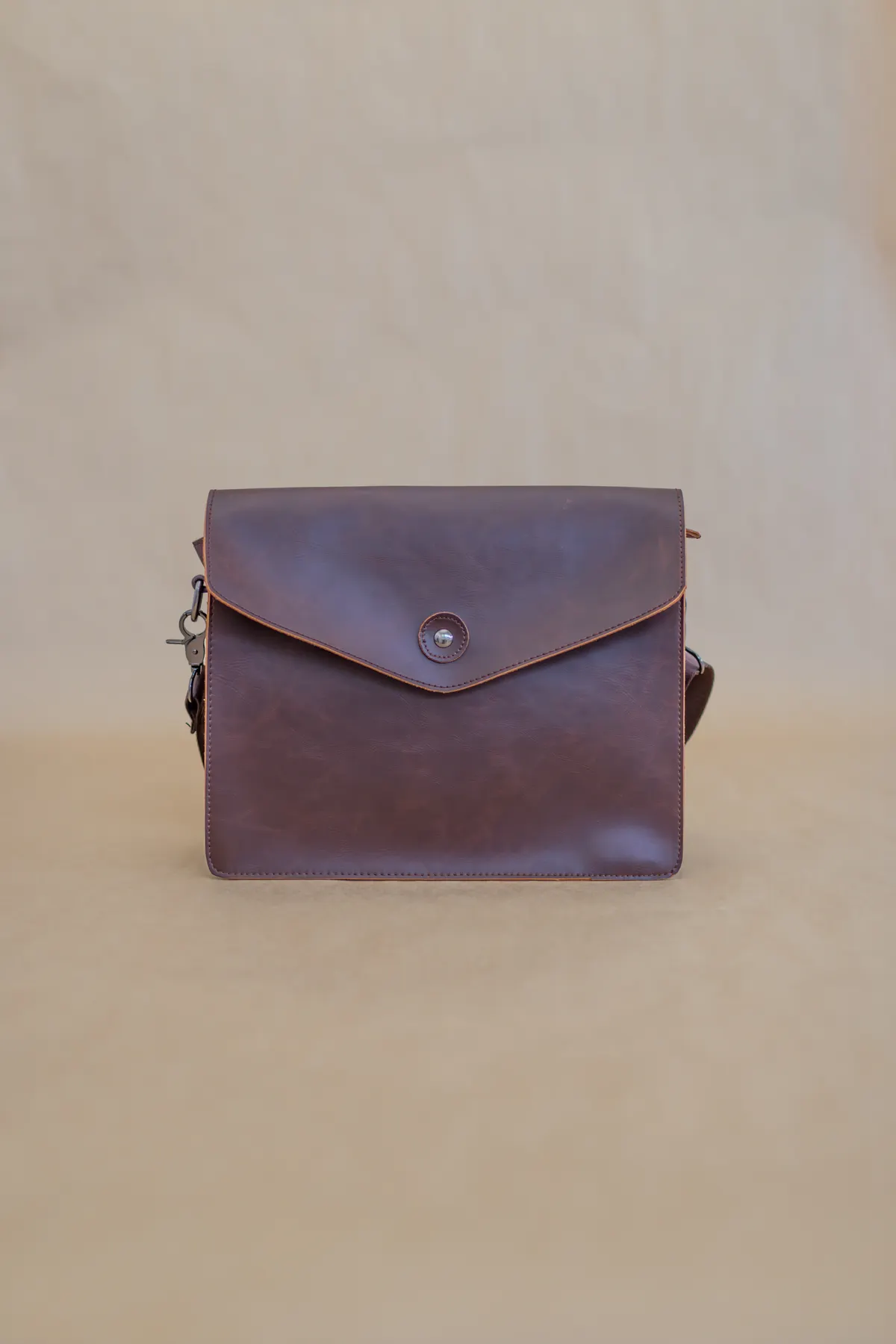 Brown leather satchel with a curved flap against a neutral background