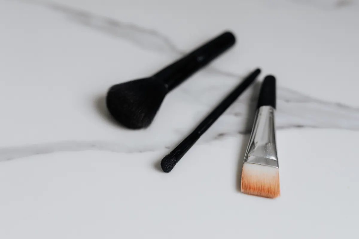 Black makeup brushes arranged on pale marble