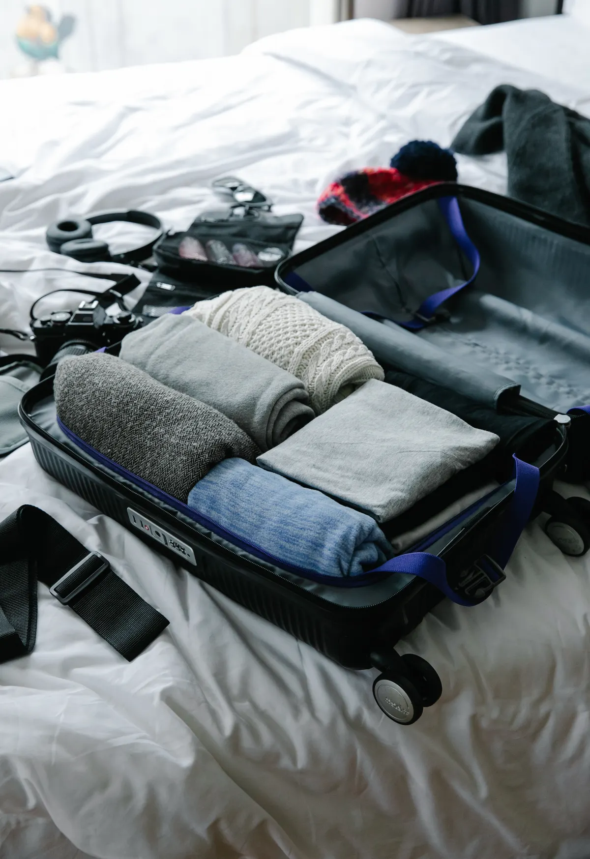 An open suitcase packed with folded clothing on a bed